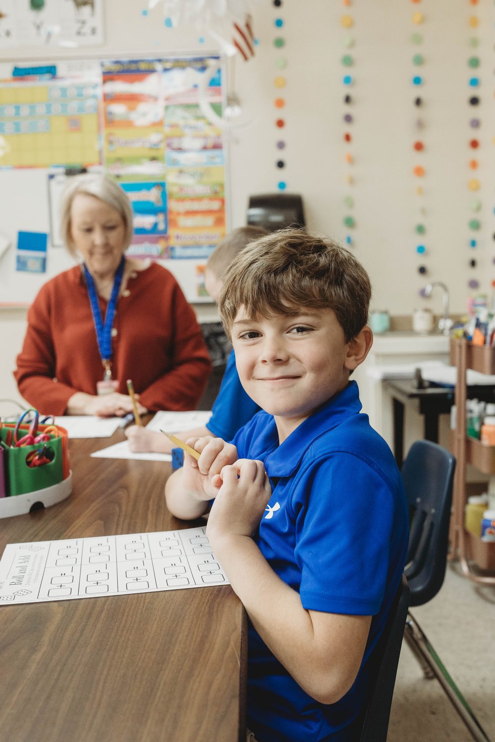 A Lower School student works at his desk alongside his teacher at Columbia Academy